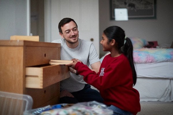 An adult helping a young person with a drawer in a room